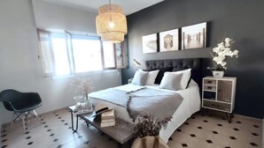 A modern bedroom with a large bed, a bedside table, a chair, a floor lamp, and a wall-mounted shelf.