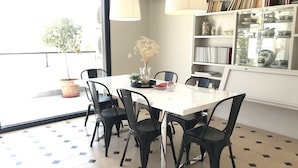 A dining area with a white table, black chairs, a potted plant, and a bookshelf with books and decorative items.