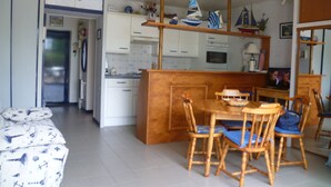 Een compacte keuken met witte kastjes, een houten eettafel met stoelen en een klein eiland.