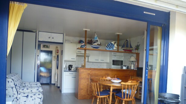 Een keuken met witte kasten, een houten eettafel met stoelen en een klein schiereiland met een spoelbak.