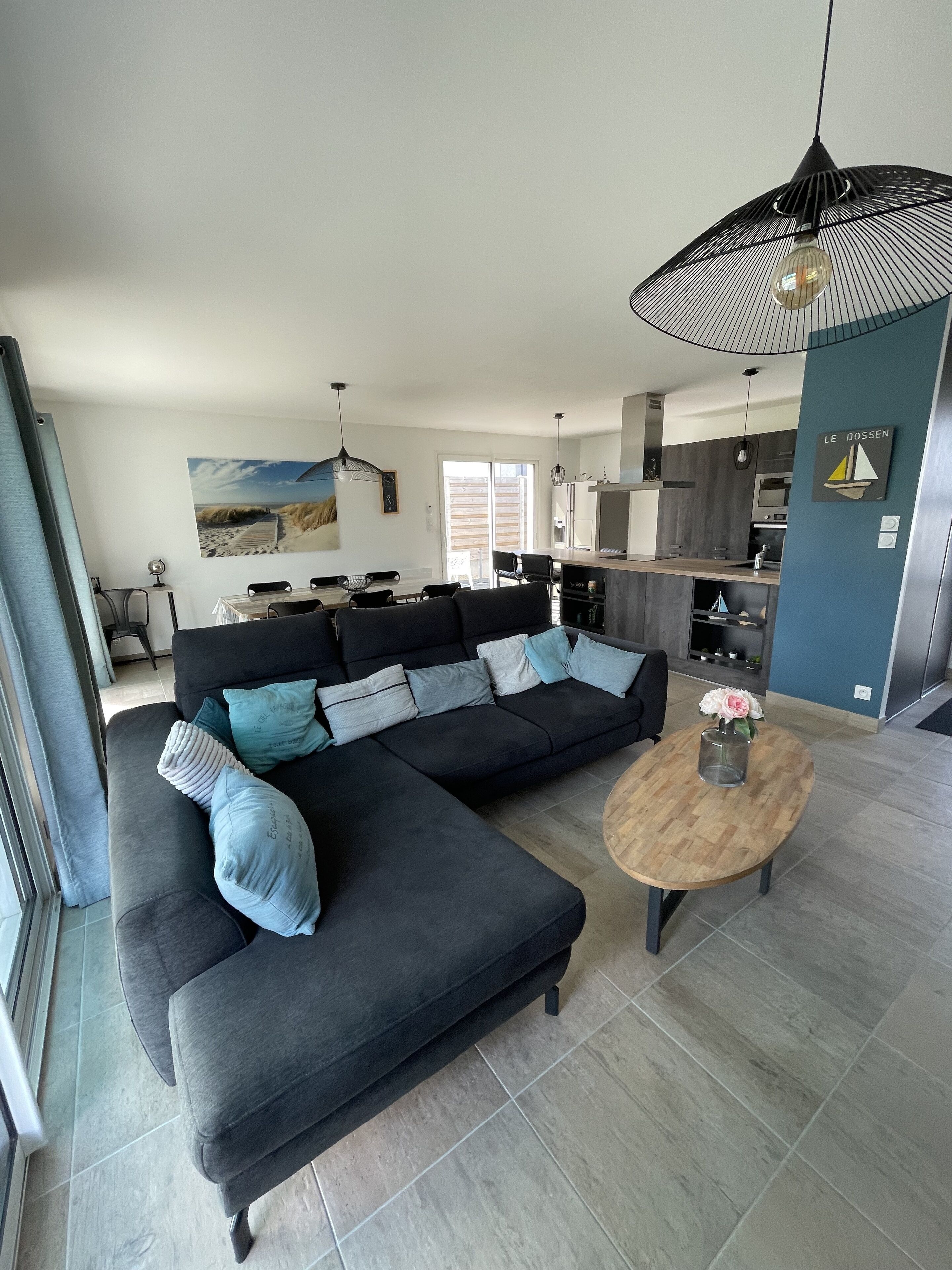 A modern living room with a dark sectional sofa, a wooden coffee table with flowers, and a large black pendant light.