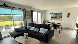 Un salon moderne avec un canapé noir, une table basse en bois et un coin repas comprenant une table et des chaises.