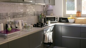 A modern kitchen with grey cabinets, a microwave, a kettle, and a window providing natural light. - Spectacular ocean views - 5 min walk to beach (Ericeira)