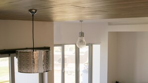 A modern living room with a teal sofa, a pink pillow, and a patterned ottoman. There is a large window with a view of the outside. - Spectacular ocean views - 5 min walk to beach (Ericeira)