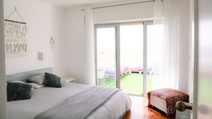 A bedroom with a bed, a nightstand, a wall-mounted light, and a sliding glass door leading to a balcony. - Spectacular ocean views - 5 min walk to beach (Ericeira)