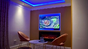 Een gezellige kamer met een wandtelevisie, een open haard en twee stoelen.