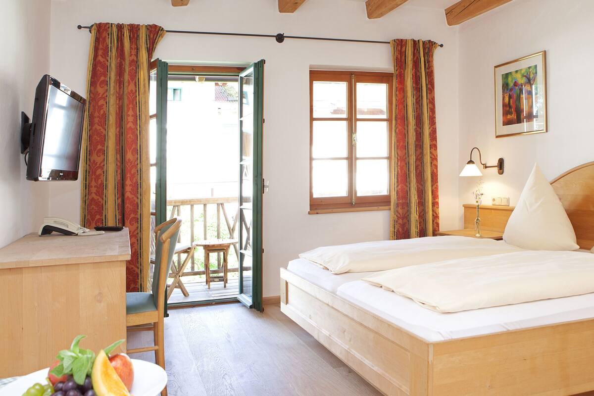 A hotel room with a wooden bed, a desk with a telephone, a television, and a window with curtains.