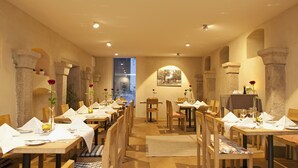 En restaurant med træborde og -stole, stensøjler og udsigt over bybilledet gennem et stort vindue.