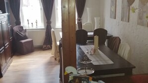 A dining area with a wooden table, chairs, and a window with curtains. There is a wicker basket with magazines and a small table with a candle. - Glori * s apartment (Bad Sooden-Allendorf)