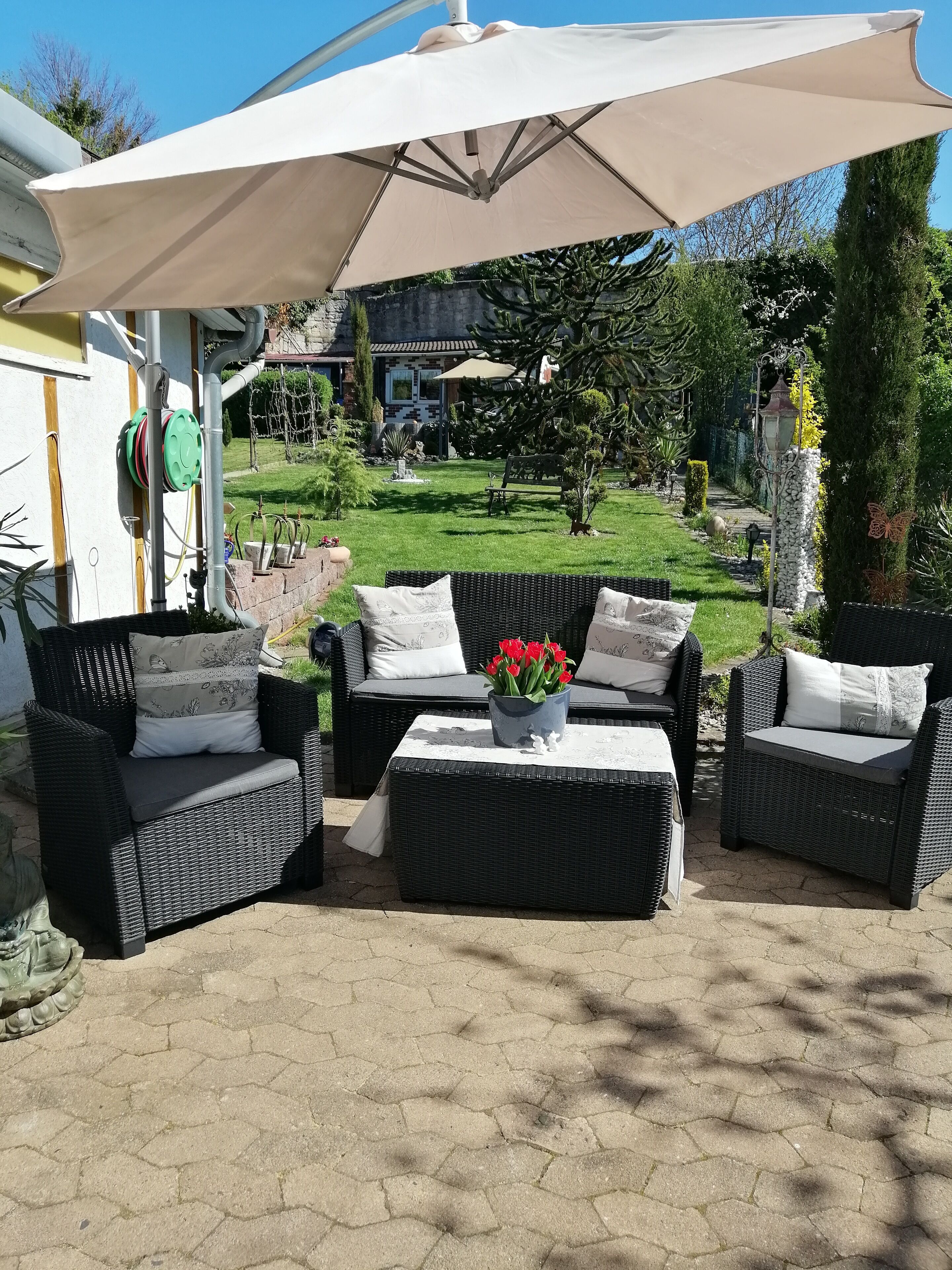 An outdoor patio area with wicker furniture, a large umbrella, and a garden view.