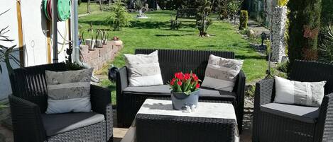 An outdoor patio area with wicker furniture, a large umbrella, and a garden view.
