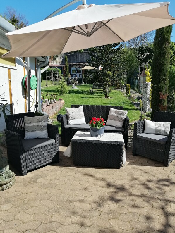 An outdoor patio area with wicker furniture, a large umbrella, and a garden view. - Glori * s apartment (Bad Sooden-Allendorf)