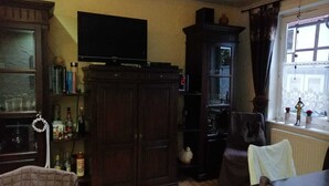 A living room with a dark wooden cabinet, a television on top, a bookshelf, and a window with curtains. - Glori * s apartment (Bad Sooden-Allendorf)