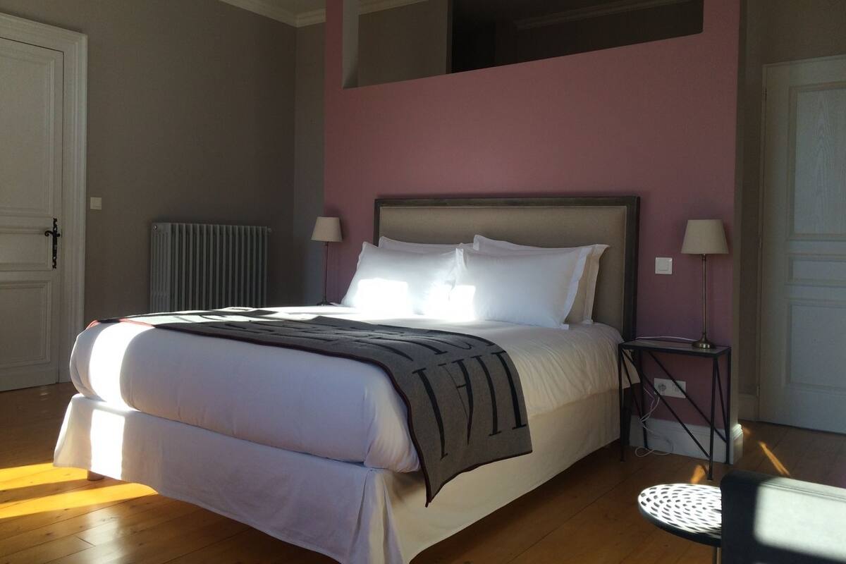 A bedroom with a bed, bedside lamps, a radiator, and a window.