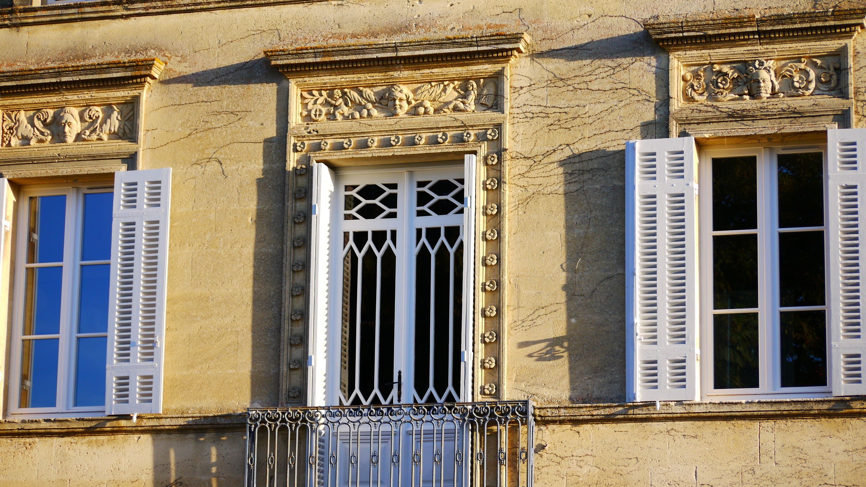 Fachada de edifício com três janelas, cada uma com portão e molduras decorativas.