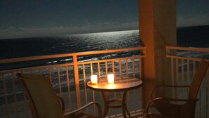 Un balcón con mesa y sillas, con vistas al océano de noche.