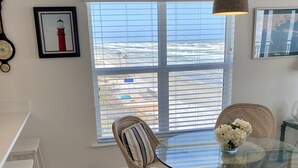 Comedor con sillas de mimbre, una mesa de vidrio y vista al océano a través de amplios ventanales.