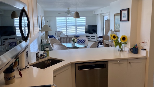 Una cocina moderna con lavavajillas, un comedor con mesa de vidrio y una sala de estar con sofá y televisor.