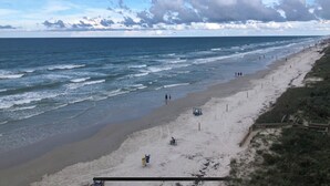 Una playa con orilla arenosa, algunas personas caminando y un cielo despejado con nubes.