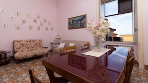Una habitación con una mesa de comedor, sillas, un sofá, un florero con flores, un cuadro en la pared y una ventana con vistas.