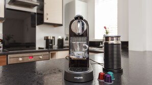 Una cocina con una cafetera moderna, un dispensador de agua y un recipiente de acero inoxidable sobre la encimera.