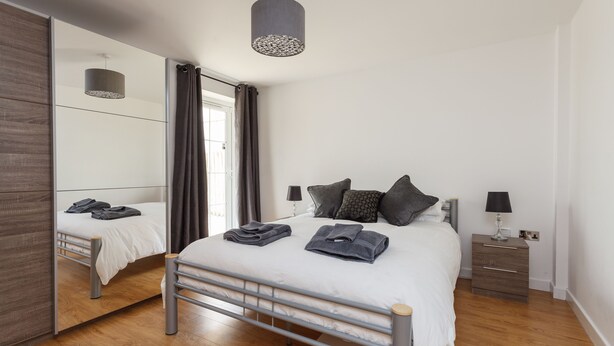 Un dormitorio moderno con cama, mesitas de noche, un espejo y una lámpara colgante.