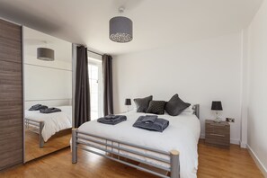 A modern bedroom with a bed, bedside tables, a mirror, and a hanging light fixture. - Stunning Contemporary Apartment (Bournemouth)