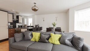 Una sala de estar moderna con un sofá gris, un comedor y una cocina al fondo.