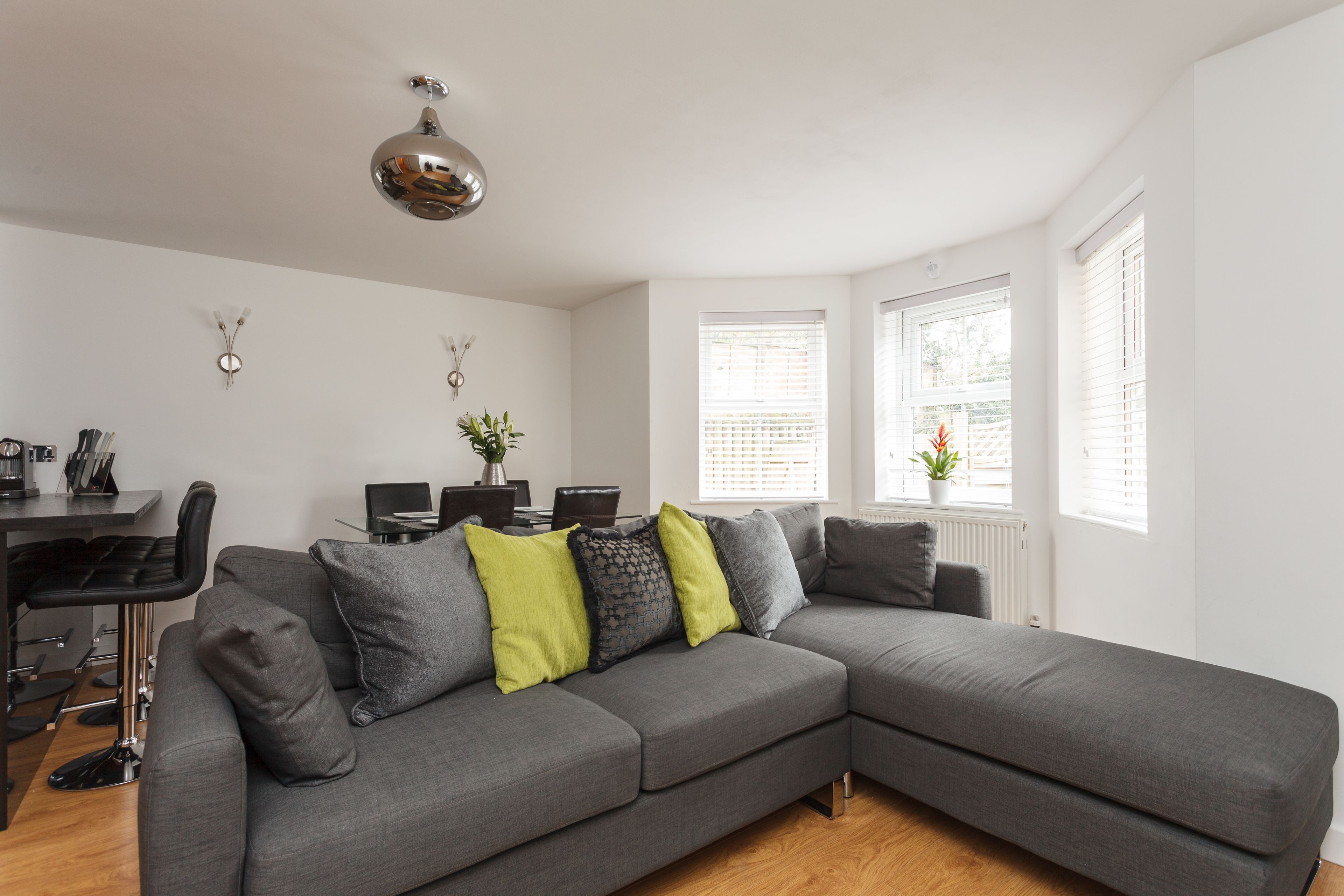 Ein modernes Wohnzimmer mit einem grauen Ecksofa, einem Essbereich mit Tisch und Stühlen sowie einer Pendelleuchte.