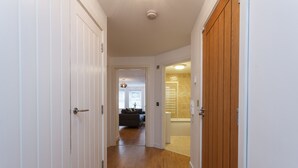 Un pasillo con suelo de madera, paredes blancas y una puerta que da a una sala de estar con un sofá y una mesa de centro.