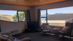 Uma sala de estar com lareira, um sofá, duas poltronas e vista para colinas e água.