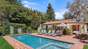 A pool with a tiled border, a covered patio area with lounge chairs, and a building with a tiled roof.