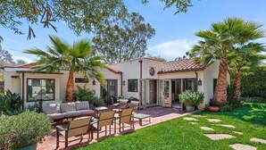 A two-story house with a patio, outdoor seating, and palm trees.