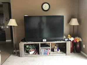 Relax in this cozy living space with a large flat-screen TV, shelves for books and decorative items, and comfortable seating.