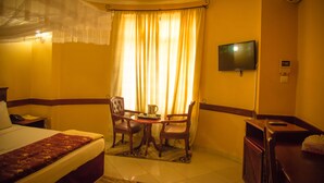 Habitación de hotel con cama, escritorio con teléfono, televisor en la pared y ventana con cortinas.