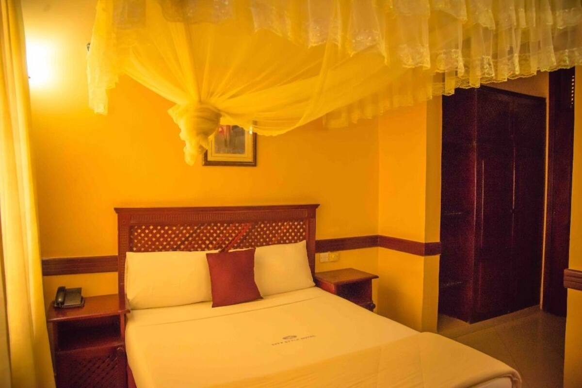 Ein Hotelzimmer mit Bett, Holz-Kopfteil, Nachttischen und einem gelben Vorhang.