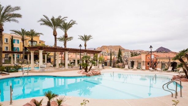Una piscina con palmeras, una zona cubierta y edificios al fondo.