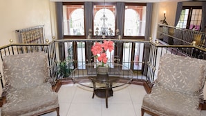 Un balcón amplio con una mesa de vidrio, dos sillones estampados y un jarrón de flores.