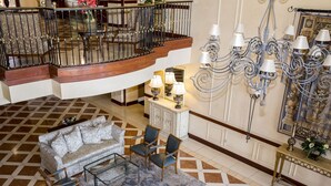 Un vestíbulo espacioso con techo alto, una escalera monumental, un candelabro y un área de descanso con sofá y sillones.