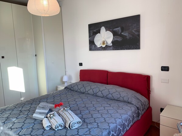A neatly made bed with a patterned bedspread, red headboard, and rolled towels with star decorations.