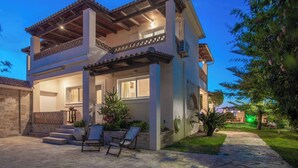 Une maison à deux étages dotée d’un patio couvert, d’un espace salon extérieur et d’un jardin bien entretenu.