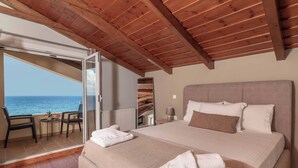 Une chambre avec un grand lit, une vue sur la mer et un balcon équipé de chaises et d’une table.