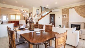 Un vaste espace de vie comprenant une table à manger en bois, des sièges confortables, une cheminée et un escalier menant à un niveau supérieur.