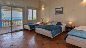 Una habitación con dos camas, una mesita con bandeja, un cuadro en la pared y vista al mar a través de una puerta corredera.
