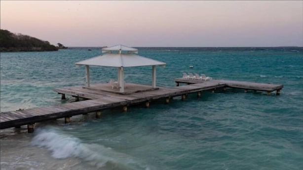 Un muelle de madera que se adentra en aguas turquesas, con un pabellón y sillas de descanso.