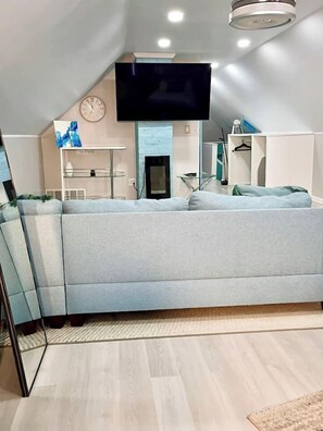 Un salon moderne avec un canapé d’angle, un téléviseur à écran plat fixé au mur, une cheminée et une petite table avec une lampe.