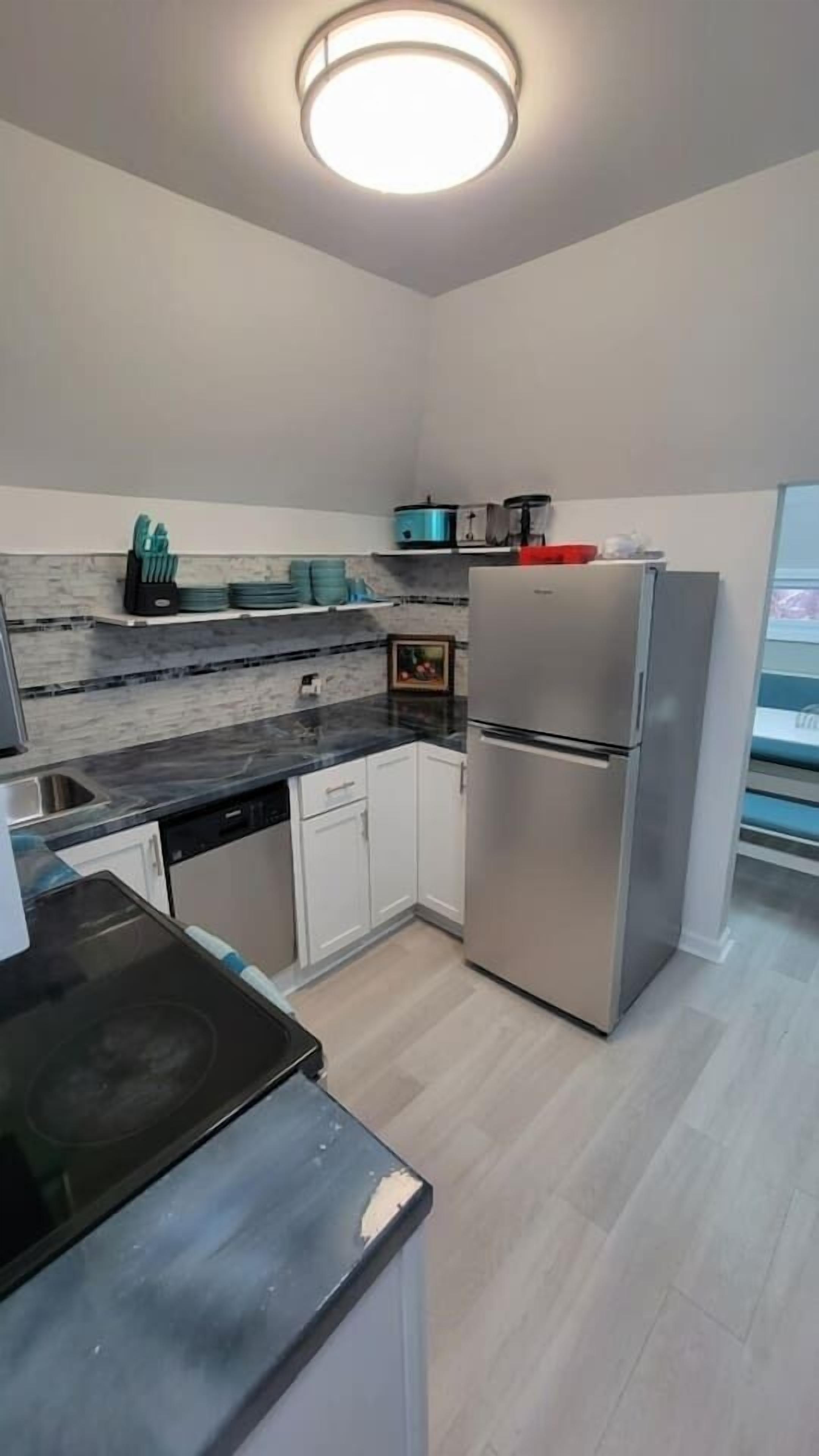 A modern kitchen with a built-in stove, stainless steel appliances, white cabinetry, and a light wood floor.