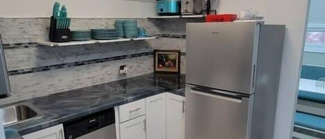 A modern kitchen with a built-in stove, stainless steel appliances, white cabinetry, and a light wood floor.