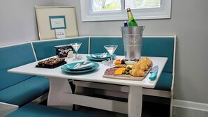 A dining area with a table set for two, featuring a bottle of champagne, a glass, a box of Breyers ice cream, a plate of cheese, olives, and croissants. - Romantic Escape to The Luxury Loft (Detroit)