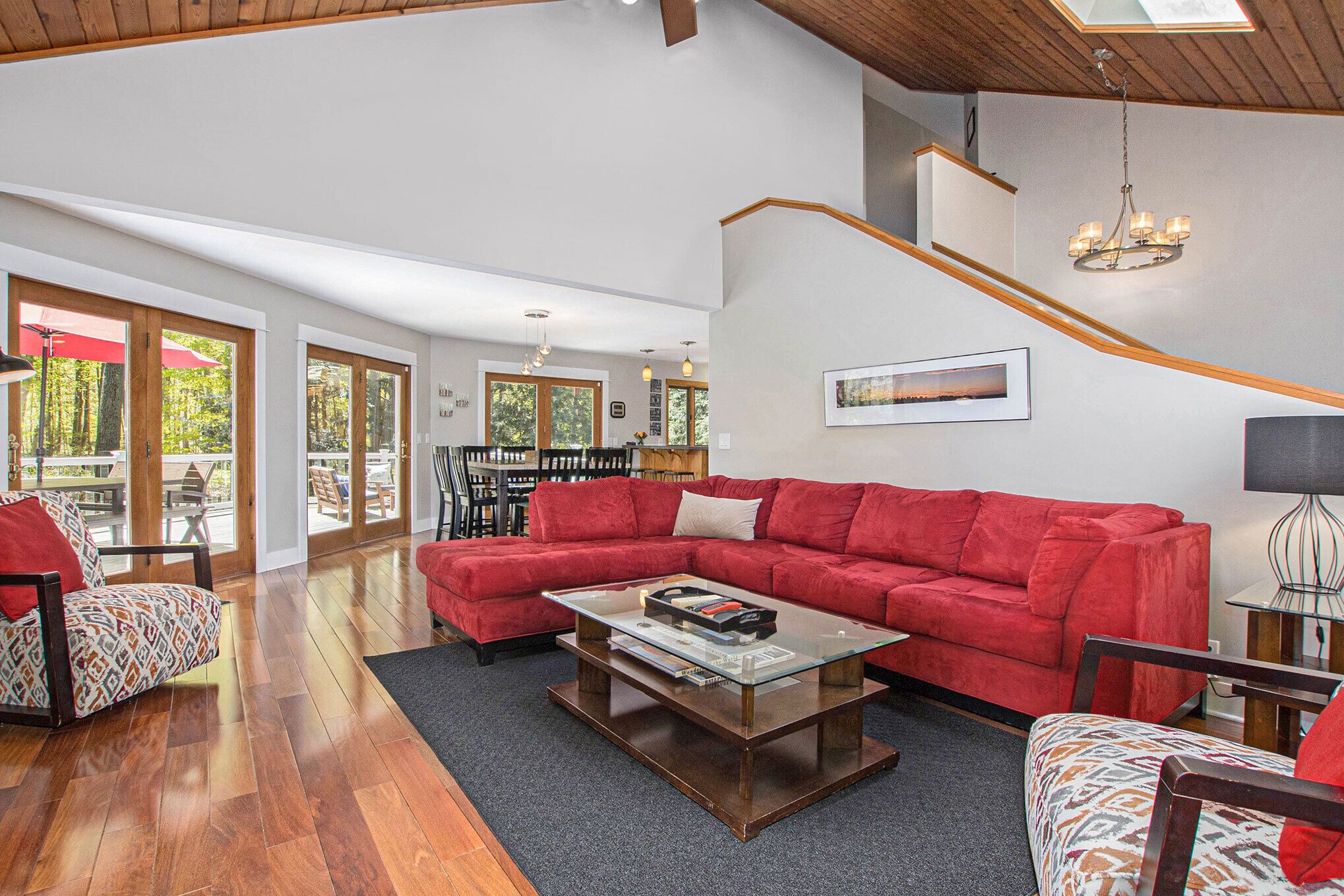 A spacious living room with a red sectional sofa, a glass coffee table, and a staircase leading to an upper level.
